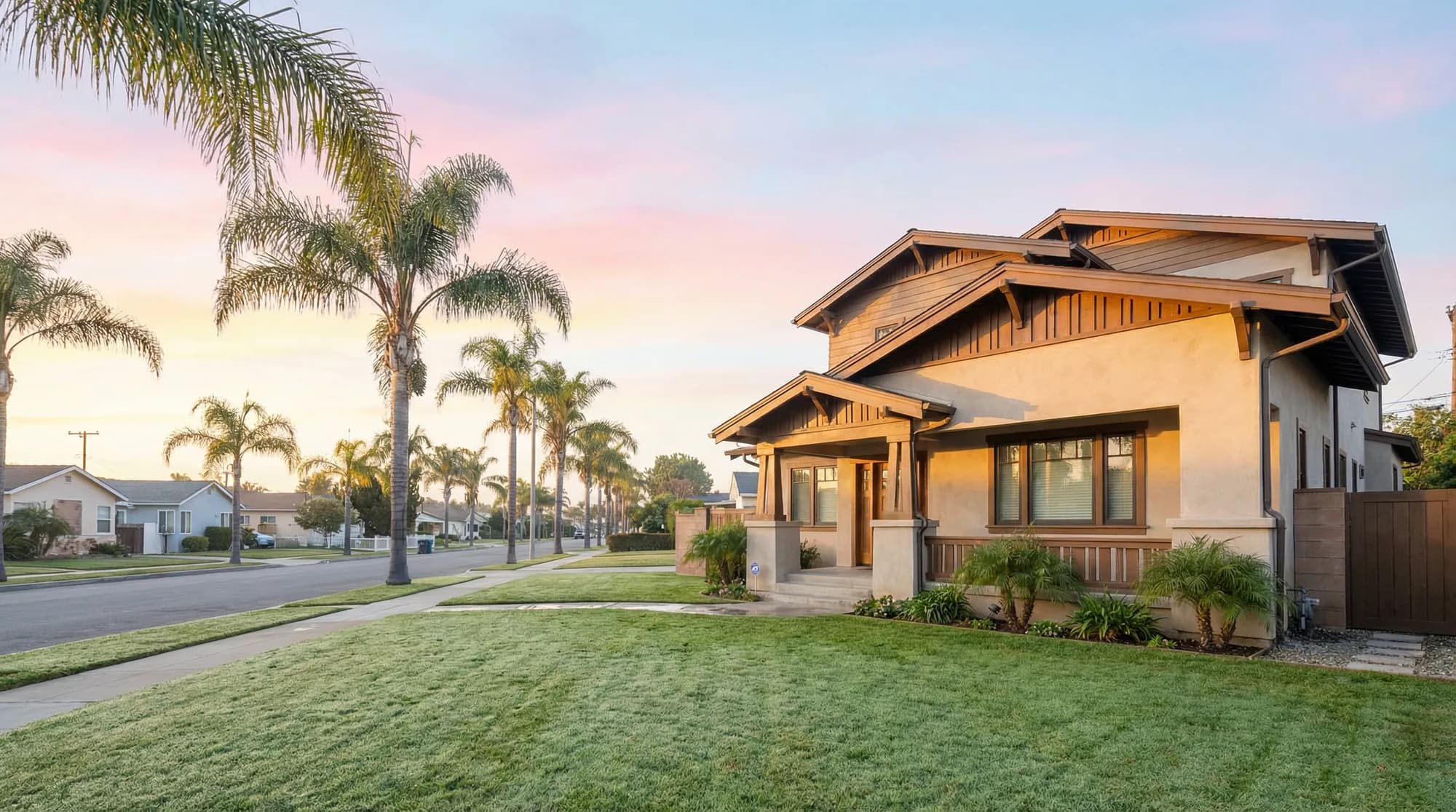 Two-story Craftsman home with a covered front porch and a green lawn on a palm-lined street in morning light